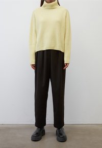Maglione a collo alto a coste di un delicato giallo pallido abbinato a pantaloni neri larghi e stivali neri chunky. L'outfit presenta un design rilassato e minimalista.