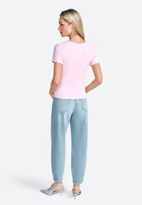 Lys pink ribbet top med scalloped ærmer, parret med lyseblå løse jeans og blege blå hælede mules, set fra ryggen.