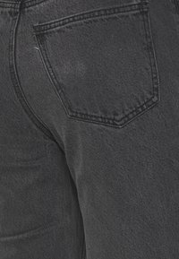 Jeans de ganga preto com um corte clássico, apresentando um bolso traseiro distinto e uma textura subtil proveniente do entrelaçado do tecido.