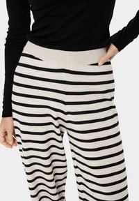 Pantalons rayés avec un doux dégradé de crème et de noir, dotés d'une large taille élastique et d'une coupe décontractée. Tissu en tricot texturé.