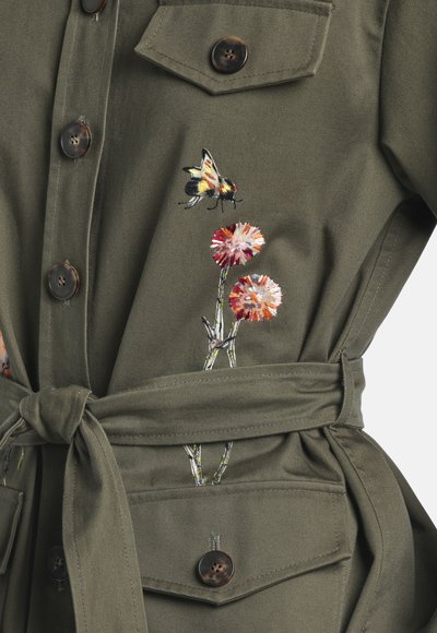 Olive green buttoned jacket with waist tie featuring embroidered bee and two pink and orange flowers near chest pocket.