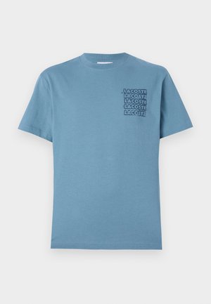 Camiseta de algodón azul claro con cuello redondo y mangas cortas. En el lado izquierdo del pecho tiene un diseño del logotipo apilado en negro "LACOSTE".