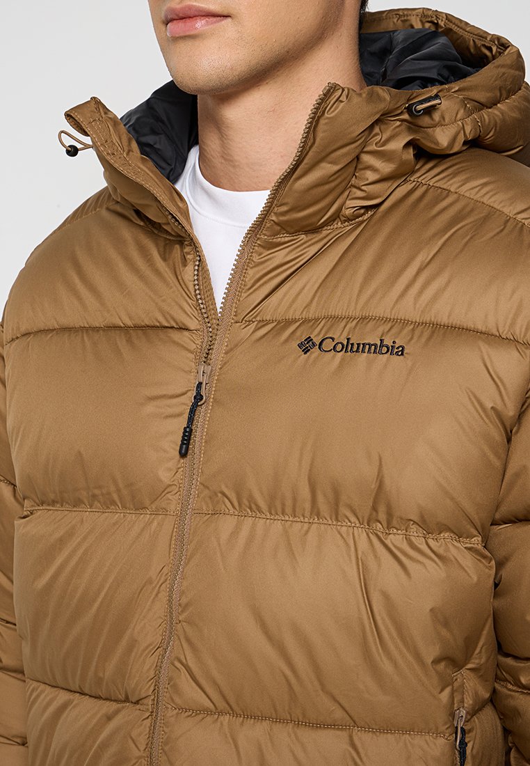 Veste en doudoune marron avec zip à l'avant, capuche et logo Columbia. Elle présente une texture lisse et un motif cousu pour l'isolation.