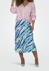 Vaaleanpunainen pitkähihaisten nappipaita yhdistettynä virtaavaan siniseen midi-hameeseen, jossa on monivärinen aallokkomuoto. Harmaat korkokengät.