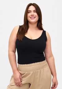 Svart ärmlös bodysuit med rundad hals och sömlöst design, i kombination med beige byxor med samlad midja gjorda av lättviktsmaterial.