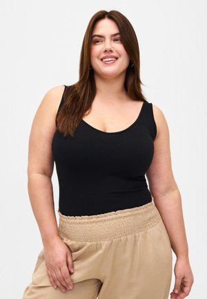 Schwarzer ärmelloser Bodysuit mit Rundhalsausschnitt und nahtlosem Design, kombiniert mit beigen, gerafften Bund-Hosen aus leichtem Material.