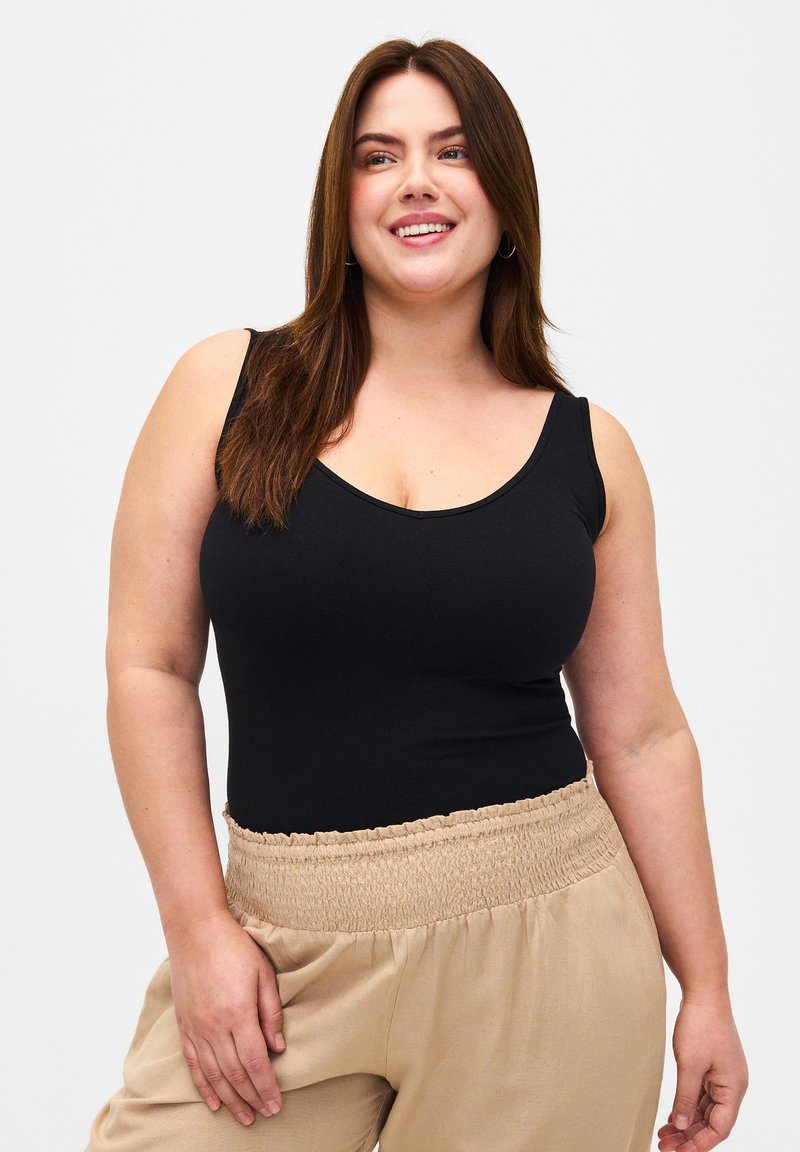Svart ärmlös bodysuit med rundad hals och sömlöst design, i kombination med beige byxor med samlad midja gjorda av lättviktsmaterial.