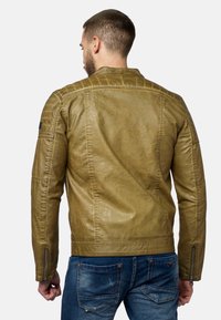 Giubbotto di pelle marrone con una finitura texturizzata, polsini con zip e un taglio dritto. Indossato sopra jeans blu, che mostrano un aspetto casual.