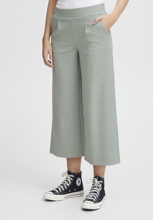 Groen geblokte wijde broek met voorzakken, gecombineerd met zwarte hoge sneakers. De broek heeft een textuurpatroon over de gehele stof.