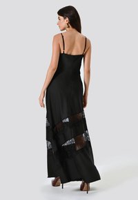 Zwarte maxi-jurk met verstelbare spaghettibandjes, voorzien van kanten panels en een gladde afwerking. Valt elegant en is stijlvol te combineren met hooggehakte schoenen.