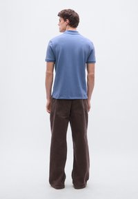 Īsroku zila polo krekls no mīksta auduma ar klasisku apkakli un sānu šķēlumiem, kopā ar brīvām brūnām korduroja biksēm.