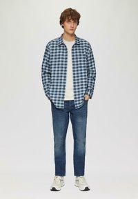 Blauwe en witte geblokte overhemd, lichtgrijs T-shirt, donkerblauwe jeans en lichte sneakers. Casual fit met knoopsluiting en lange mouwen.
