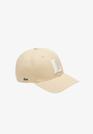 Gorra de béisbol beige con una letra "L" blanca bordada en la parte frontal y un pequeño logo de cocodrilo verde en el lateral.