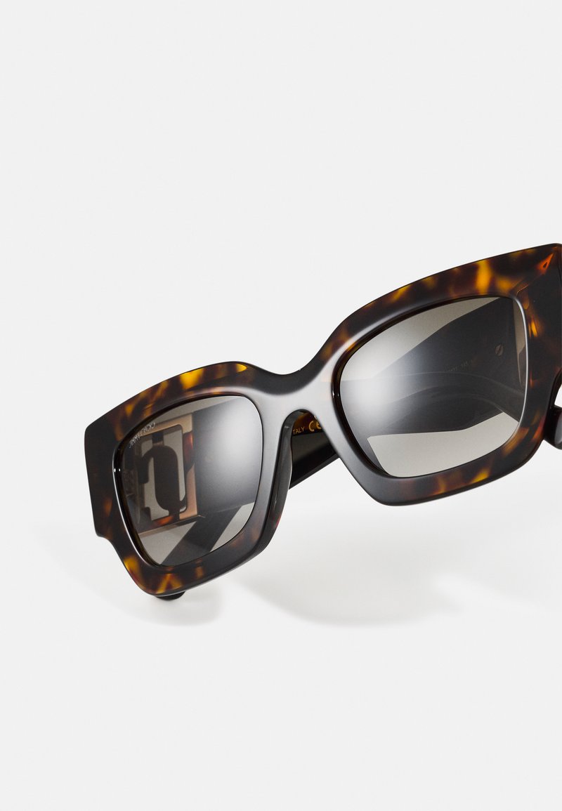 Lunettes de soleil en écaille de tortue avec des montures rectangulaires surdimensionnées et des verres dégradés. Fini lisse avec un léger éclat et un design robuste.