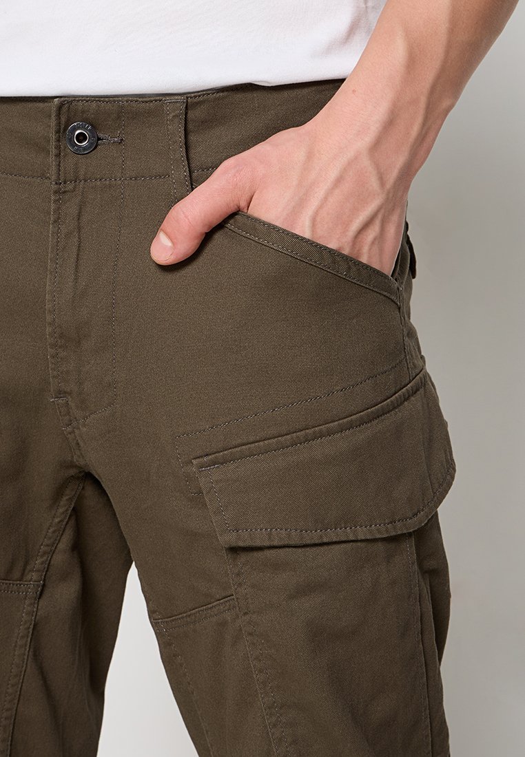 Pantalones cargo de color verde olivo, fabricados con tejido resistente, que cuentan con bolsillos laterales, un bolsillo frontal con botón y costuras reforzadas.
