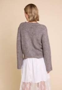 Grå, fluffy genser med lange ermer, en avslappet passform, og en litt cropped bakdel, kombinert med et hvitt blondeskjørt. Myk tekstur, uformell design.