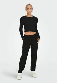 Crop top nero a costine con maniche lunghe, abbinato a pantaloni neri larghi. Sneakers bianche completano il look. Design minimalista, texture elegante.