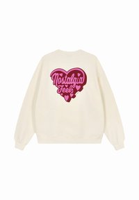 Felpa di colore crema con una grande grafica a forma di cuore rosa sul retro, accompagnata dal testo "Nostalgia Feels" e cuoricini più piccoli.
