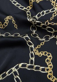 Tissu noir avec un motif de chaînes dorées aux maillons intriqués. Texture lisse ; le design comprend des chaînes entrelacées de différentes formes.