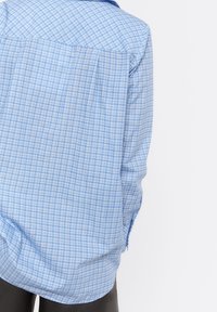 Camicia a quadri blu e bianca, maniche lunghe, colletto abbottonato, con vestibilità morbida, caratterizzata da un orlo curvo e una texture in cotone soffice.