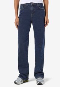 Tamsiai mėlynos tiesios kojų džinsai su penkių kišenių dizainu ir subtiliais siuvinėjimo akcentais. Dėvimi su pilkais sportiniais batais.