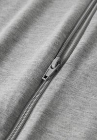 Tissu gris zippé au toucher lisse. La fermeture éclair est gris clair, dotée d'une tirette et de coutures visibles le long des bords.