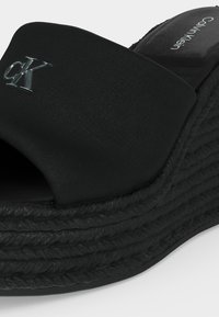 Μαύρο σανδάλι τύπου σλάιντ με πλατφόρμα από την Calvin Klein με υφασμάτινο πάνω μέρος, ασημένιο λογότυπο "cK" στο λουράκι και υφή στην σόλα.