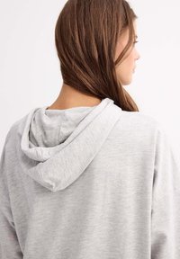 Sudadera gris con un tejido suave y texturizado, que presenta una gran capucha y costuras de hombro caídas, mostrada desde atrás.