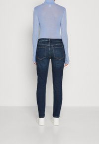 Tajta, mörkblå denimjeans med hög midja och klassiska bakfickor. Matchat med en ljusblå, långärmad topp.