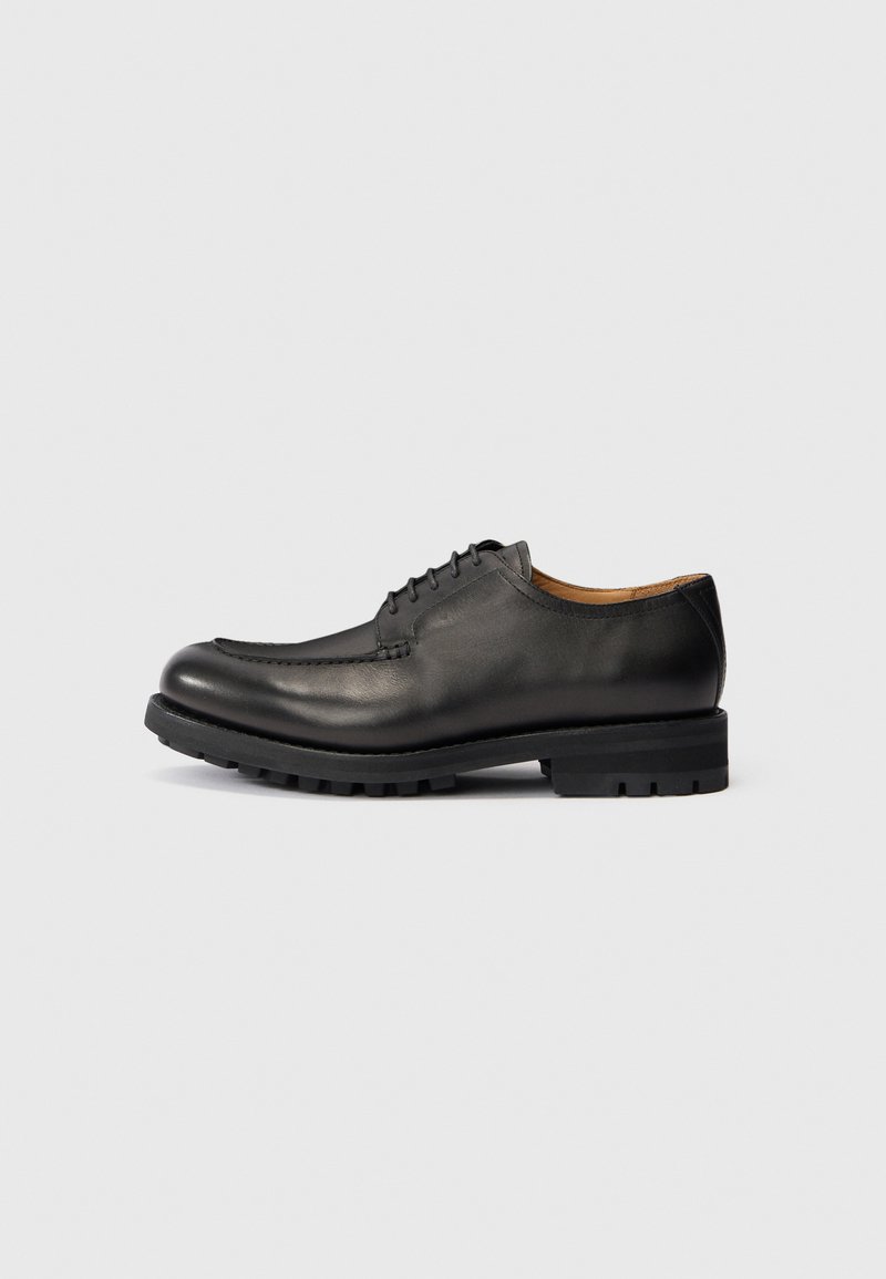 Zwart leren veterschoen met dikke robuuste zool en ronde neus, zijaanzicht op een plain lichte achtergrond.