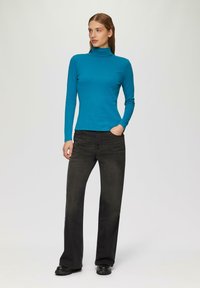 Turquoise langemouw turtleneck-shirt gecombineerd met high-waisted zwarte jeans en zwarte schoenen met dikke zolen. Glad materiaal, aansluitend ontwerp.