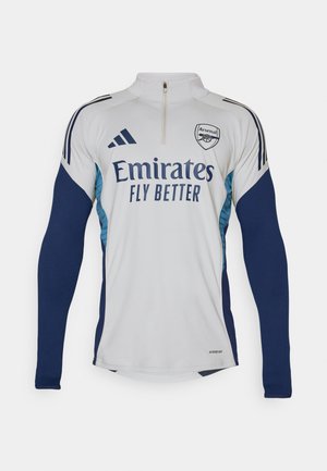 Hvid langærmet trøje med marineblå detaljer, halv-zip halsudskæring, med "Emirates Fly Better" logo og Arsenal klublogo.