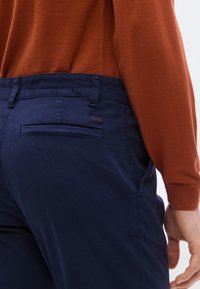 Marinblå manchesterbyxor med en bakficka som har en liten märkesetikett och ett slätt midjeband, kombinerade med en rostfärgad tröja.