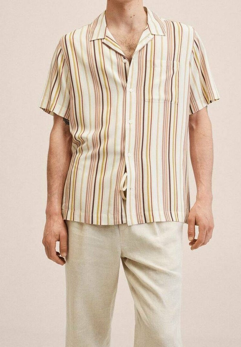 Homme portant une chemise à manches courtes boutonnée avec des rayures verticales jaunes, marron et beige, associée à un pantalon beige clair.