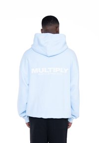Sudadera con capucha de color azul claro y corte relajado. Presenta un audaz texto blanco "MULTIPLICAR" y "MULTIPLICAR CLUB DE ROPA" en la parte posterior. Material suave.