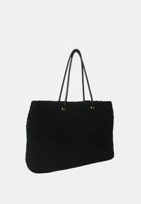 Borsa tote nera con texture, dotata di due manici in pelle sottili e occhietti in metallo dorato, su uno sfondo chiaro e semplice.