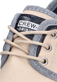 Zapatillas de lona beige con acentos de mezclilla, ojales de metal redondos y cordones beige. Presenta la etiqueta "CREW-ORIGINAL" en la lengüeta.