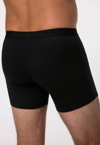 Černé bavlněné boxerky s těsným střihem. Elastický pás má jemně embosované logo. Hladký povrch, žádné viditelné vzory ani akcenty.