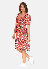 Floral jurk tot de knie met grote rode en witte bloemen op een marineblauwe achtergrond, met puffmouwen en een gerimpelde taille, gecombineerd met witte sneakers.