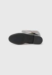 Black leather boot viewed from the bottom, featuring a smooth sole and a decorative gold buckle on the side. Simple white background.