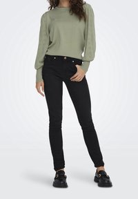Vaaleanvihreä neulepusero, jossa on teksturoituja, puffattuja hihoja; yhdistetty mustiin skinny-farkkuihin ja mustiin loafer-kengiin, joissa on kultainen yksityiskohta.
