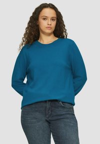 Teal langmouwtrui van zacht materiaal, met een ronde hals en een relaxte pasvorm, gecombineerd met donkere jeans. Eenvoudig, naadloos ontwerp.
