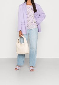 Blazer viola chiaro sopra un top floreale, jeans dritti blu chiaro, sandali con tacco lavanda e una morbida borsa beige. Texture liscia nel complesso.