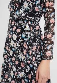 Vestido negro de flores con mangas largas y un lazo en la cintura. Presenta margaritas rosas y blancas, tela suave y un detalle de dobladillo con volantes.
