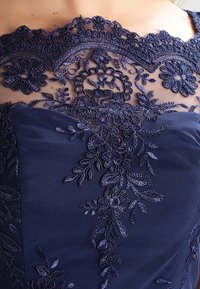 Abito da donna in navy caratterizzato da un intricata ricamo in pizzo floreale e un scollo trasparente, con un tessuto liscio e texturizzato sul corsetto.