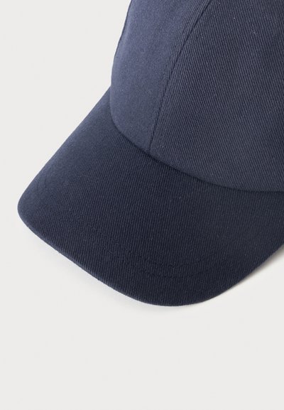 Casquette de baseball en tissu bleu foncé avec des coutures visibles sur la visière courbée et les panneaux, sur un fond clair uni.