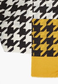 Tissu à motif pied-de-poule noir et blanc et noir et jaune avec des bords effilochés sur un fond blanc.