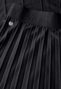 Zwarte geplooide rok met een textuurband en geborduurde "MEMORIES" en een zilveren knoopdetail. Gladde stof, elegant ontwerp.
