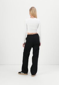 Svarta cargo-byxor med stora sidofickor i kombination med en vit åtsittande långärmad topp. Outfiten har en kortad design och en slät textur.