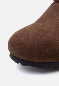 Κοντινή λήψη από τη μύτη ενός καφέ δερμάτινου παπουτσιού σουέντ με παχύ μαύρο καουτσούκ σόλα σε λευκό φόντο.